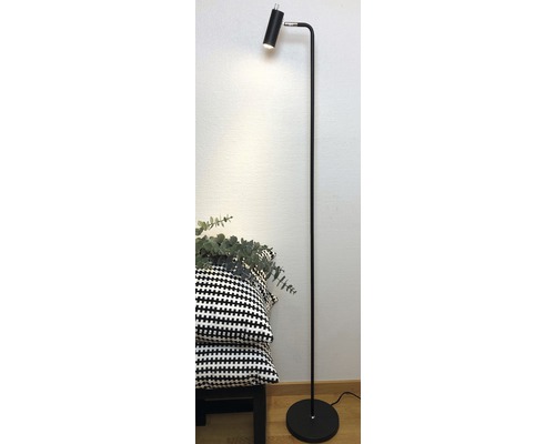 Golvlampa med justerbart lamphuvud bredvid kuddar på en pall