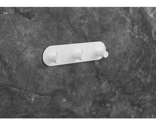 Vit vägghängare med tre krokar på en grå marmorvägg.