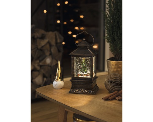 Dekorativ scen med en snöglobslykta, en tomtefigur och en krukväxt på ett bord