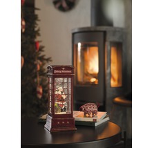 Dekorativ snöglob i form av en telefonkiosk med jultomtemotiv och öppen spis i bakgrunden.