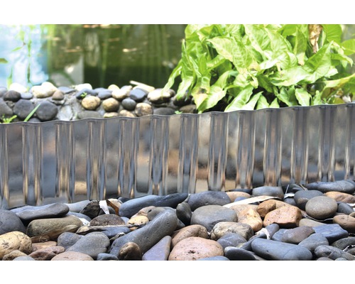 Trädgårdsscen med gräsmattekant av metall för att avgränsa en damm.