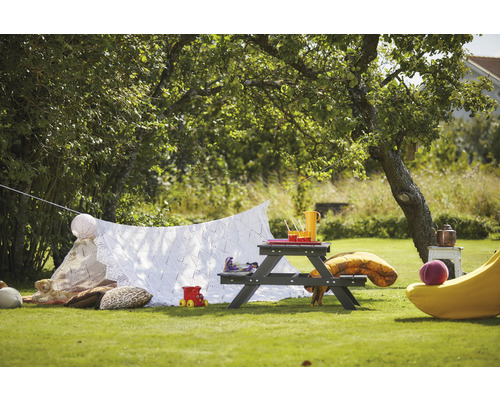 Trädgårdsscen med picknickbord, filt, kuddar och leksaker under ett träd