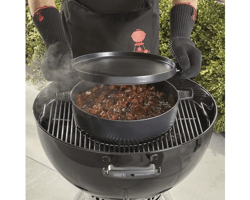 Person tillagar maträtt i holländsk ugn på en klotgrill.