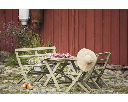 Trädgårdsmöbelset med fällbord, fällstolar och bänk framför en röd trävägg