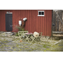 Trädgårdsscen med träbord, stolar och stråhatt framför röd trävägg