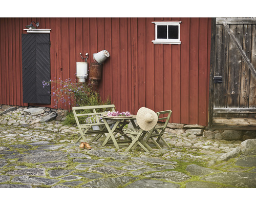 Trädgårdsscen med träbord, stolar och stråhatt framför röd trävägg
