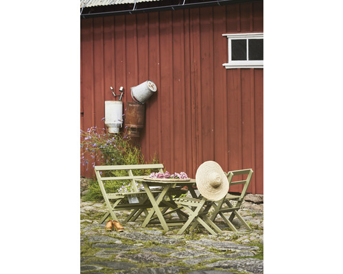 Trädgårdsscen med träbord, stolar och en stråhatt mot en röd trävägg