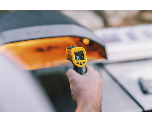 Hand håller en infraröd termometer framför en grill