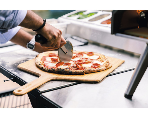 En pizza skärs på en träspade med en pizzaskärare.