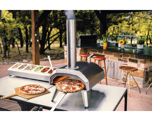 Ooni pizzaugn utomhus med pizza, ingrediensbehållare och träsked