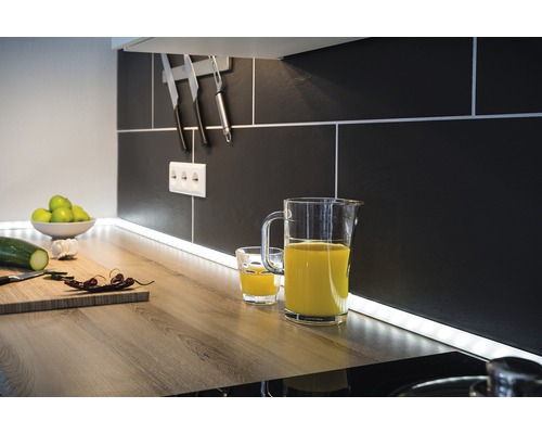 Köksscen med saftkanna, glas, skärbräda och köksredskap framför svart kakelvägg