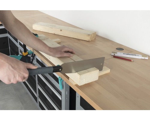 En person sågar en träbräda med en handsåg på en arbetsbänk.