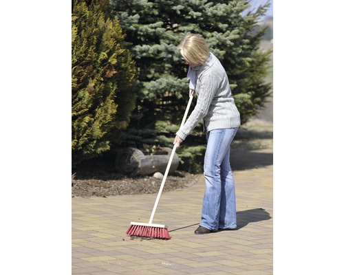 Kvinna sopar en stensatt yta i trädgården med en gatusop.