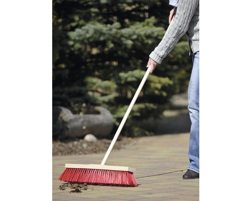 En person sopar löv på gatstenar med en gatusop.