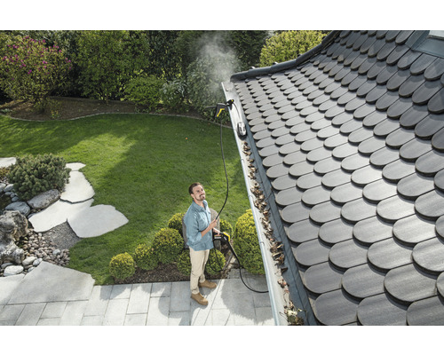 En man rengör en takränna med en högtryckstvätt i en trädgård.