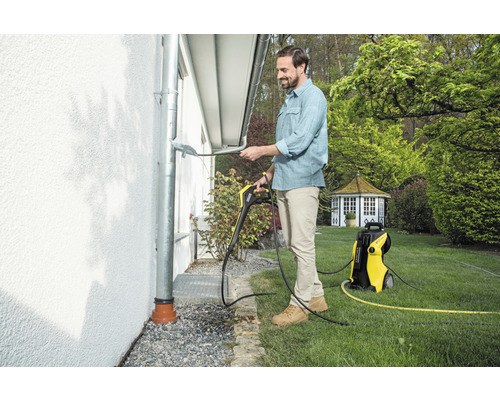 En man rengör en takränna med en Kärcher högtryckstvätt i trädgården.