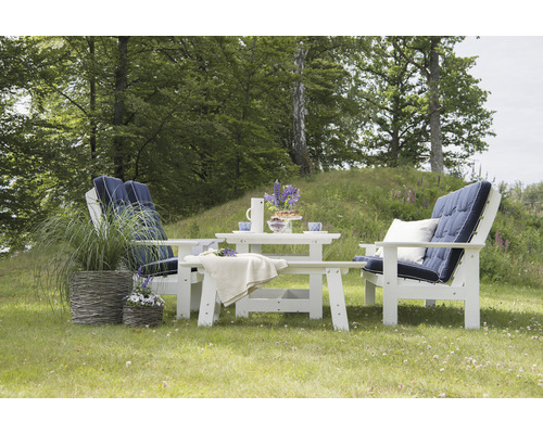 Trädgårdsscen med vita trädgårdsmöbler bestående av två stolar, ett bord och en bänk med blå dynor på en grön gräsmatta