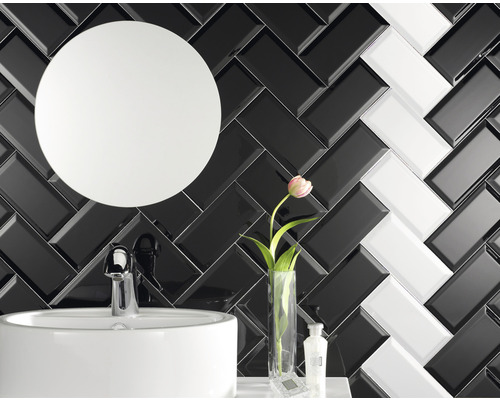 Badrumsvy med handfat, rund spegel och väggplattor i fiskbensmönster