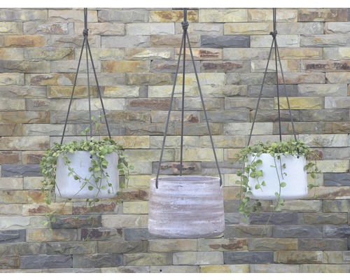 Tre hängande planteringskärl med växter framför en stenmur