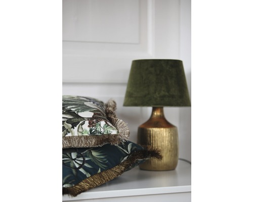 Dekorativa kuddar med fransar och en bordslampa på en hylla.