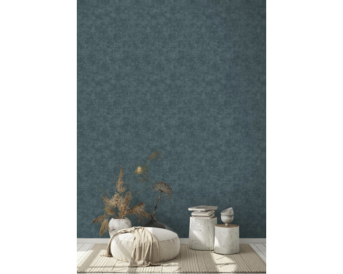 Dekorativ inredning med en puff, sidobord och torkade blommor framför en strukturerad vägg.