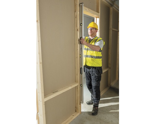 En byggnadsarbetare kontrollerar inriktningen av en dörrkarm i ett oinrett hus med ett vattenpass