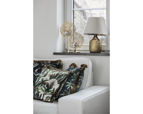 Dekorativt vardagsrum med soffa, kuddar med växtmotiv, bordslampa och värmeljushållare.