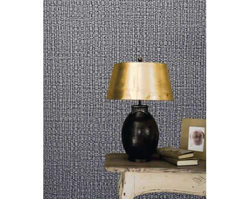 Närbild av en mönstrad tapet med ett nattduksbord, en lampa, böcker och en fotoram.