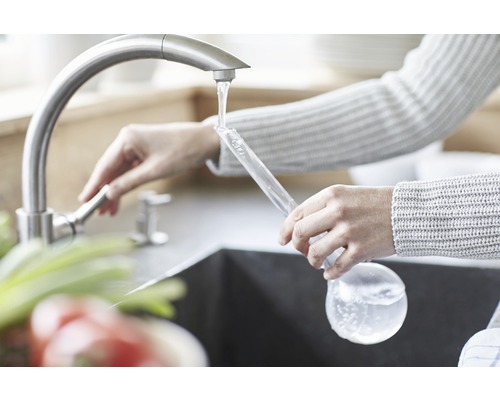 Kvinna fyller en glasflaska med vatten från kranen
