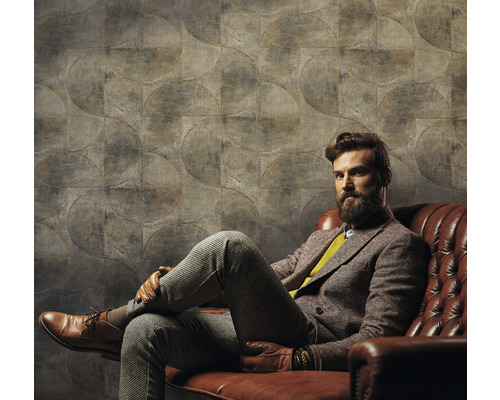 Man sitter framför en vägg med cirkelmönstrad tapet på en lädersoffa