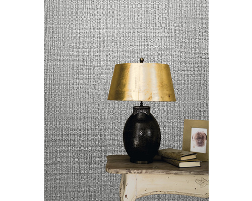 Närbild av en silverfärgad textiltapet som imiterar textilstruktur med en lampa på ett bord