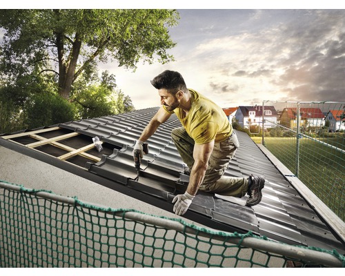 En hantverkare fäster takpannor på ett tak.