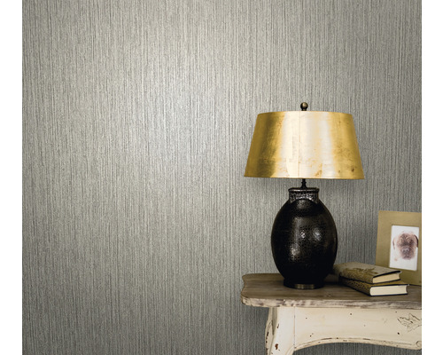 Närbild av en vägg med en tapet med en vertikal struktureffekt bredvid ett bord med en lampa, böcker och en fotoram.