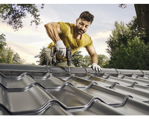 En man fäster takpannor av metall med en sladdlös skruvdragare på ett tak.