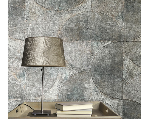 Detaljbild av en grå rumsvägg med cirkelformat tapetmönster, ett bord med en lampa och böcker.
