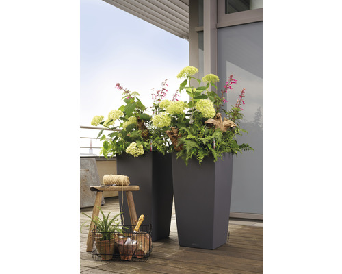 Två höga planteringskärl med blommor och växter på ett trägolv.