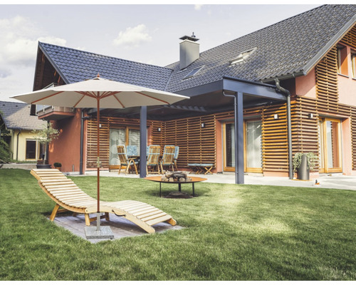 Trädgård med solstol, parasoll, sittgrupp och eldstad framför ett bostadshus.