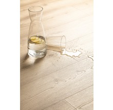 Dekorativ scen med en karaff med vatten med citronskivor och ett omkullvält glas på ett ljust trägolv