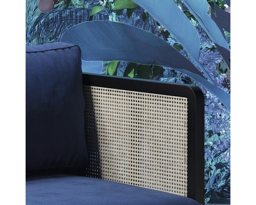 Detaljvy av en blå fåtölj med ryggstöd i rotting mot en blommig tapet