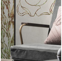 Detaljbild av en fåtölj med kudde framför en vägg med blommönster
