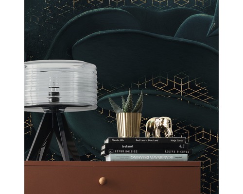 Dekorativ scen med lampa, växt, dekorativ figur och böcker på en byrå framför en mönstrad tapet