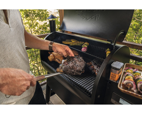Man grillar kött och grönsaker på en utomhusgrill.