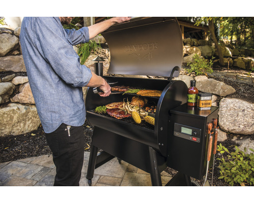 En man grillar biffar, revbensspjäll, kyckling, majs och grönsaker på en svart utomhusgrill.
