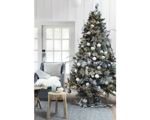 Dekorerad julgran med ljus, julgranskulor och rustika dekorationer i ett vardagsrum.