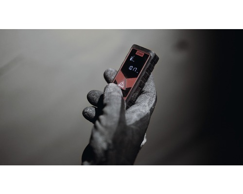 En hand med arbetshandske håller en laseravståndsmätare.