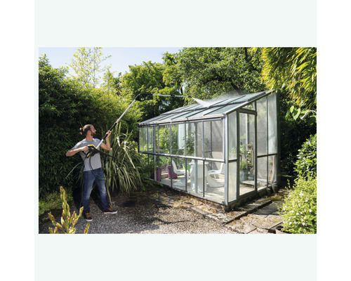 Man rengör växthus med högtryckstvätt i trädgården.