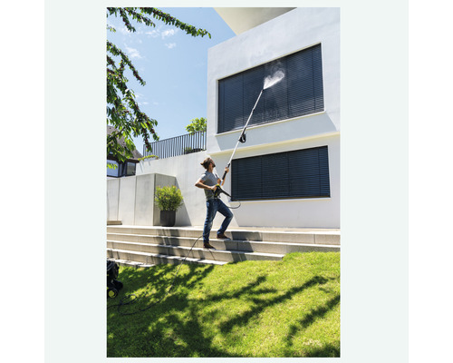 En man rengör fönstren på ett hus med en högtryckstvätt.