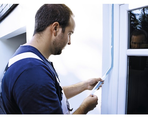 En man tejpar en fönsterkarm med maskeringstejp.
