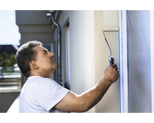 Man målar en husvägg med en färgroller.