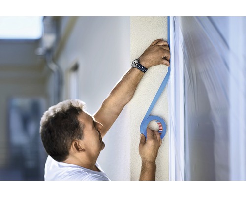 Man fäster maskeringstejp på väggen för målningsarbeten